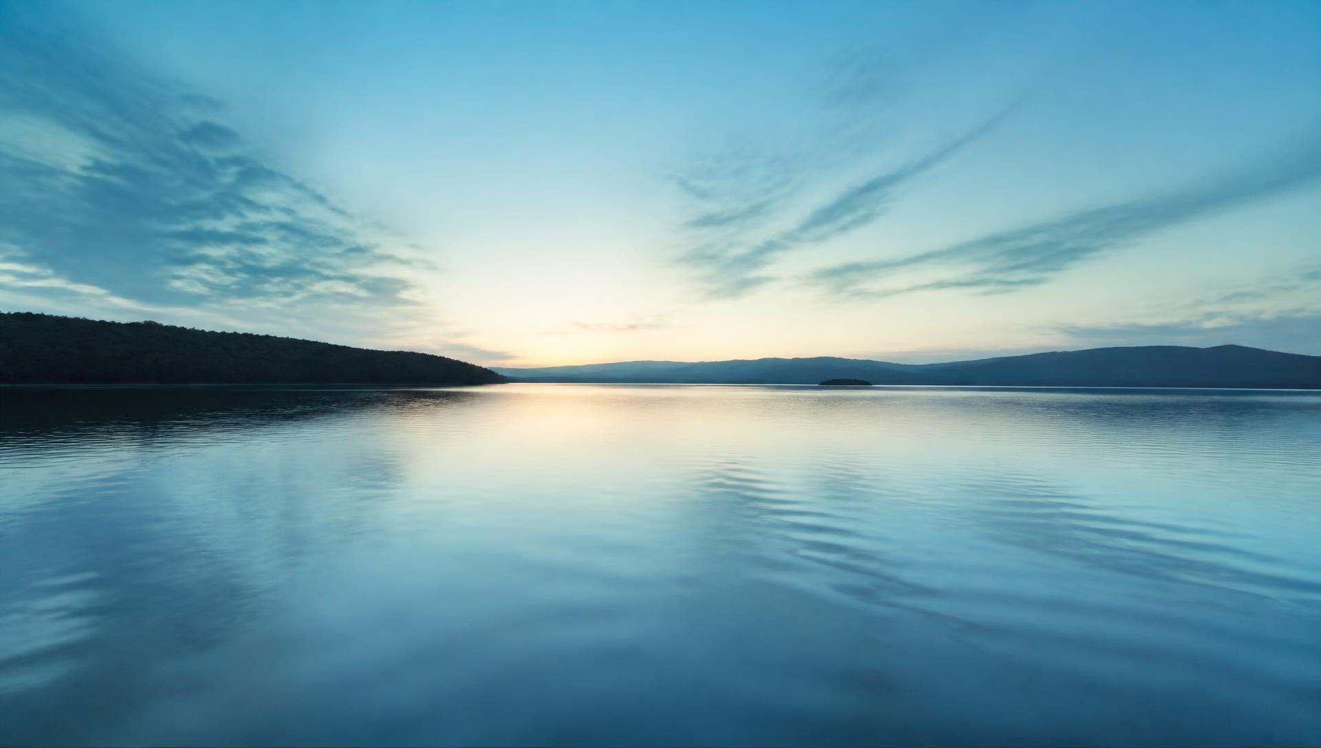 Still lake water at dawn under a pale blue sky